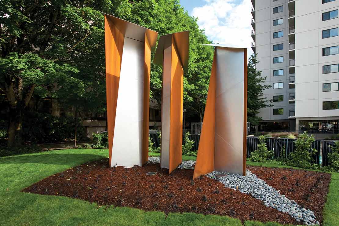 Three tall peices of stainless and weathered steel standing vertically on a field of river rock