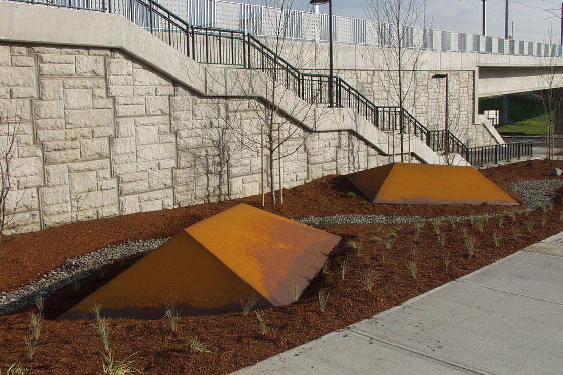 Low steel sculptures partially sunk into the landscape